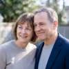 Smiling middle-aged couple standing outdoors with soft focus greenery in background.