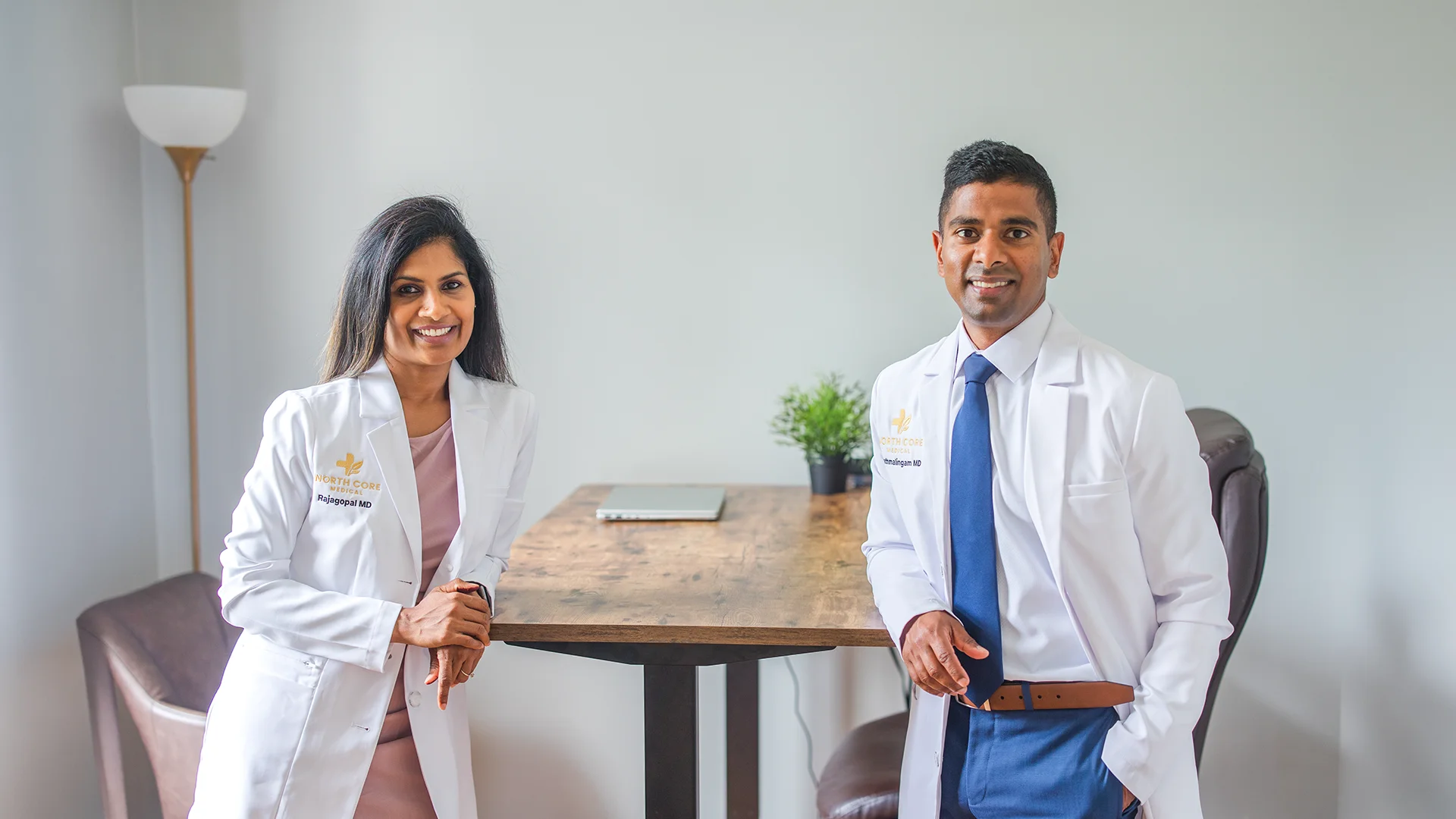 Smiling male and female doctors in white coats with stethoscopes in a medical office.