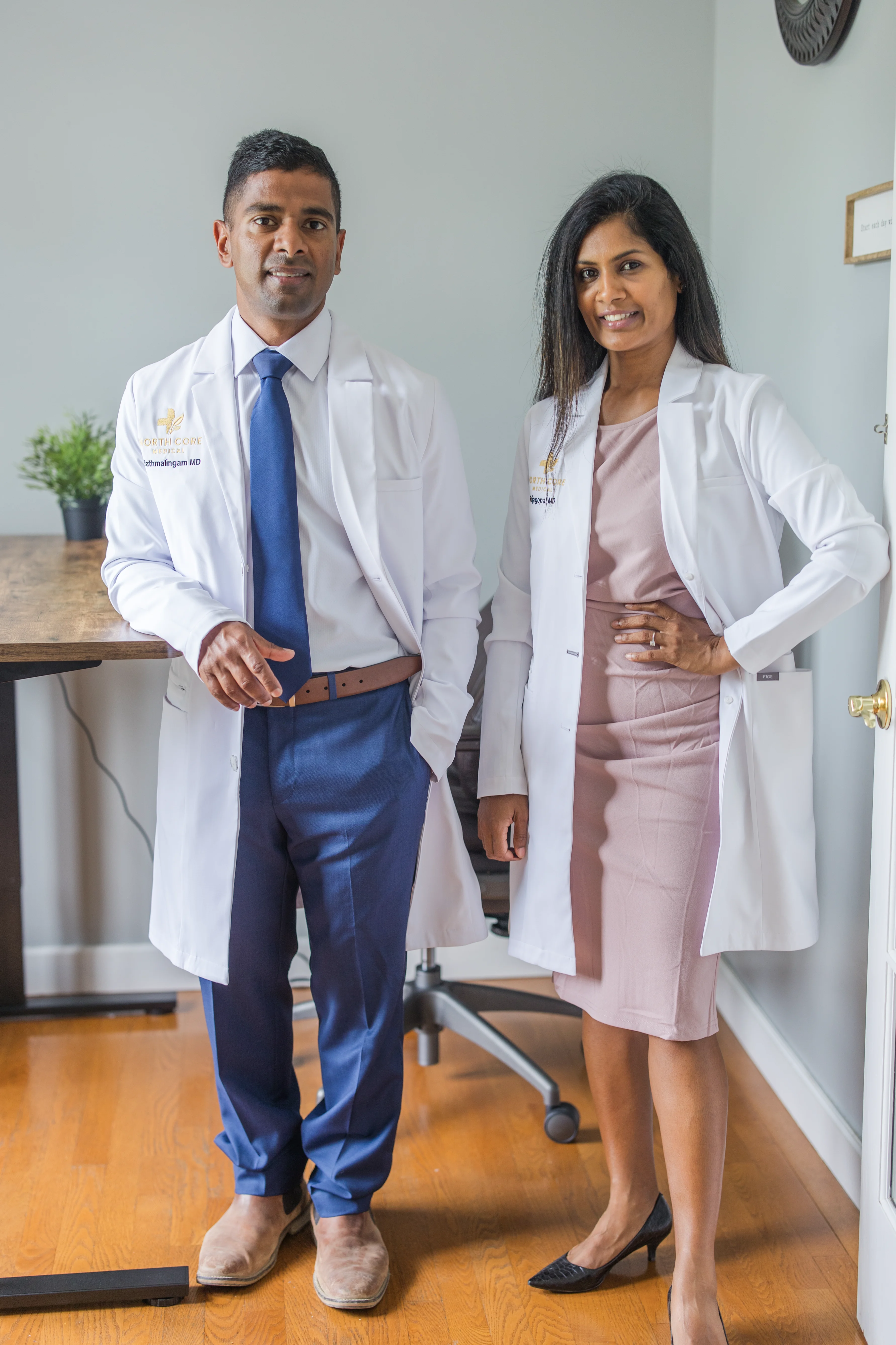 Smiling male and female doctors in white coats with stethoscopes standing indoors.