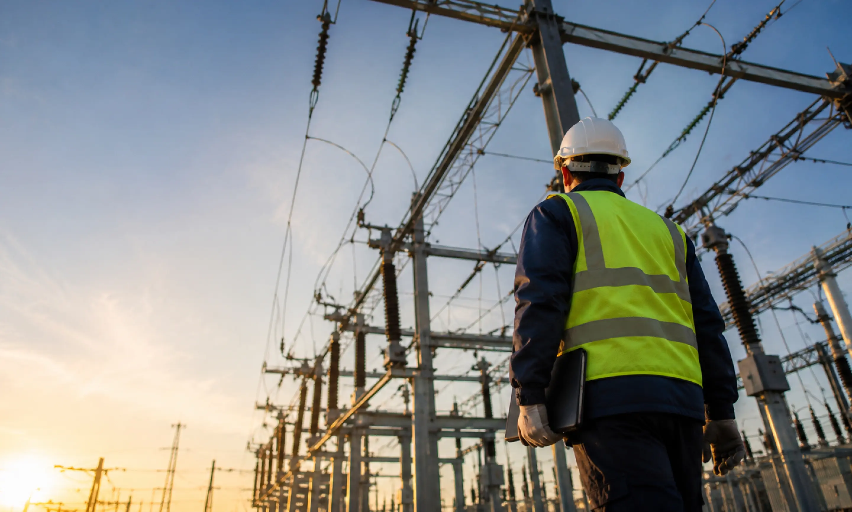 Worker in hard hat pointing toward electrical transmission towers.