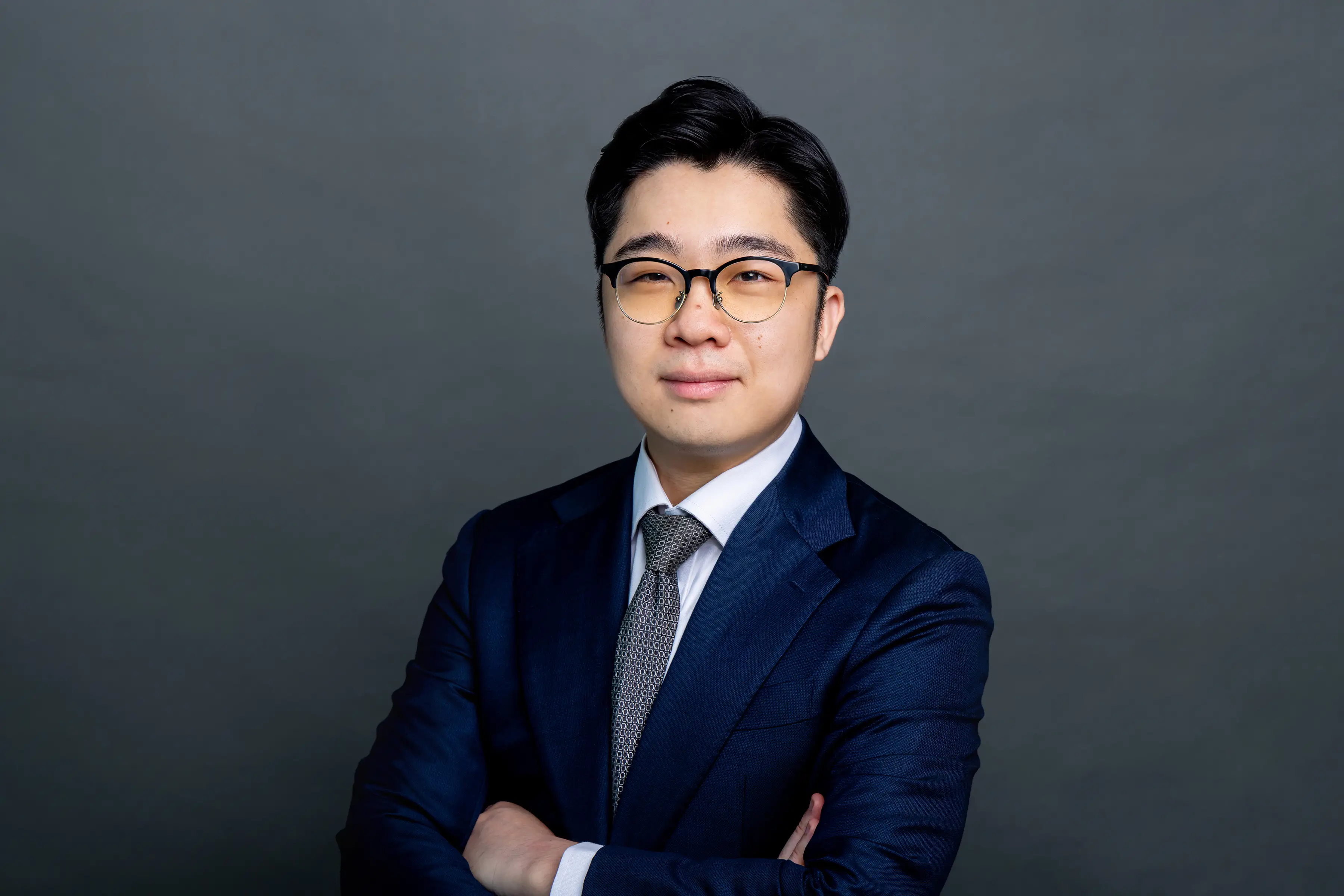 Joshua Tong, wearing a navy suit and tie against a neutral studio background.