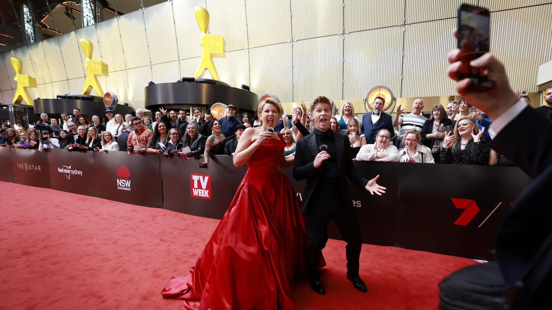 Guest in a red gown poses beside fans and photographers on the Logies red carpet.