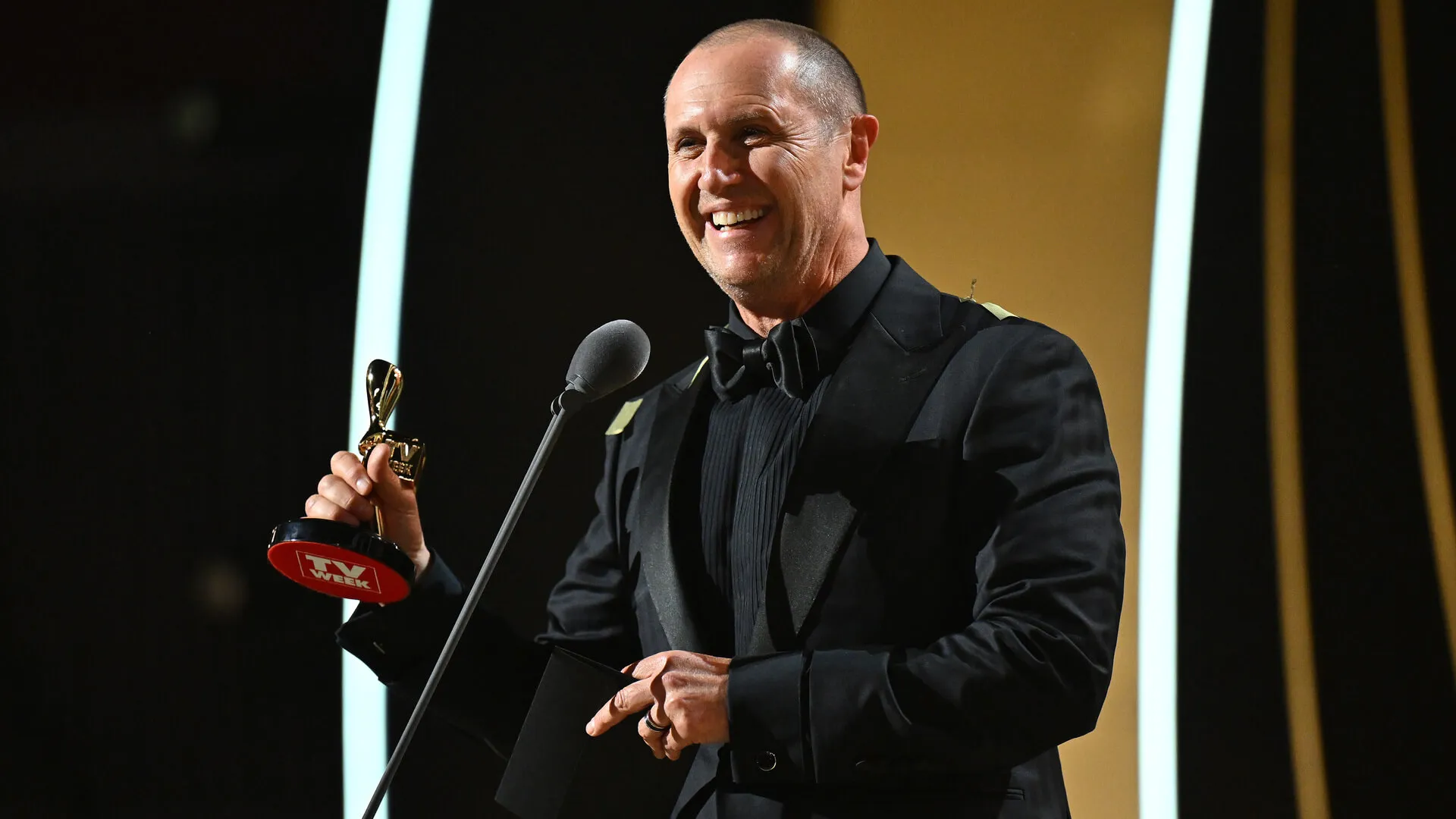 Award recipient holds a Logie trophy while speaking into a microphone.