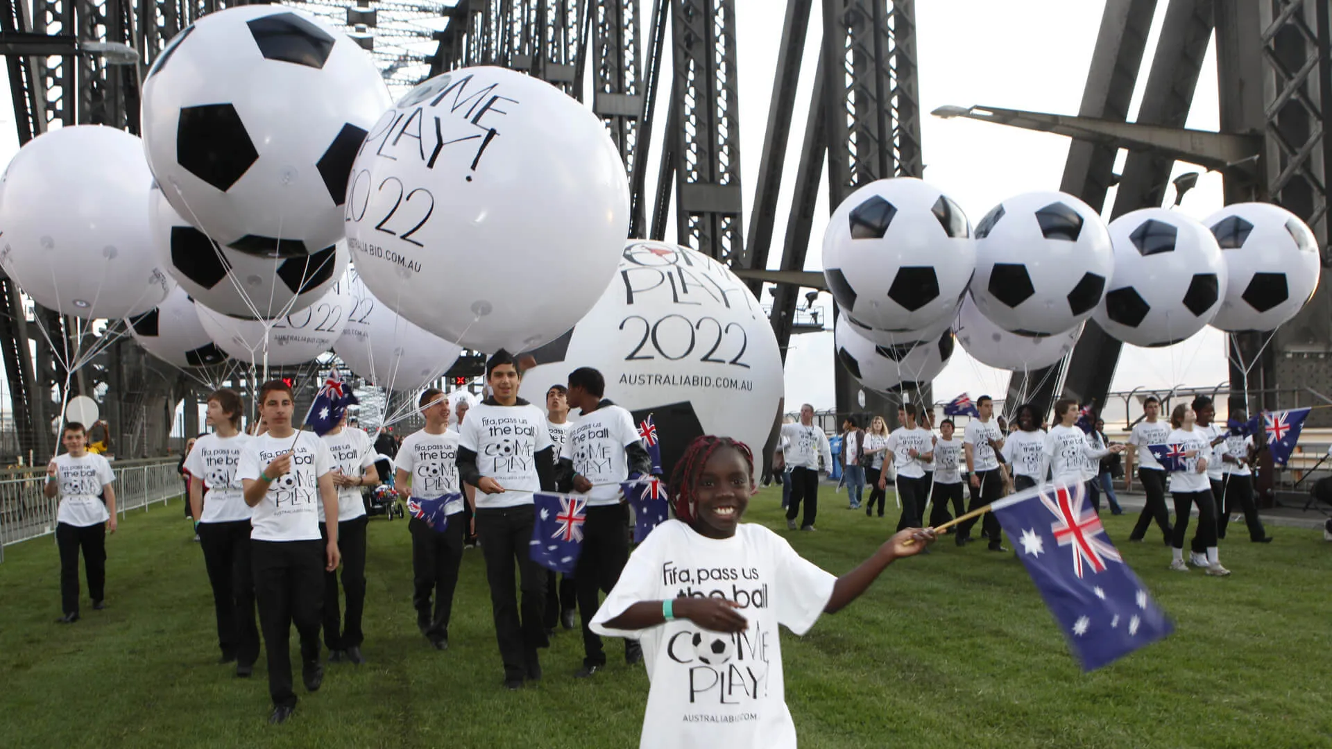 Participant stands with an Australian flag beneath oversized football balloons on the bridge.