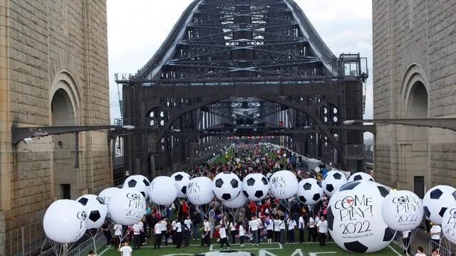 Group gathers with oversized football balloons between the Sydney Harbour Bridge pylons.