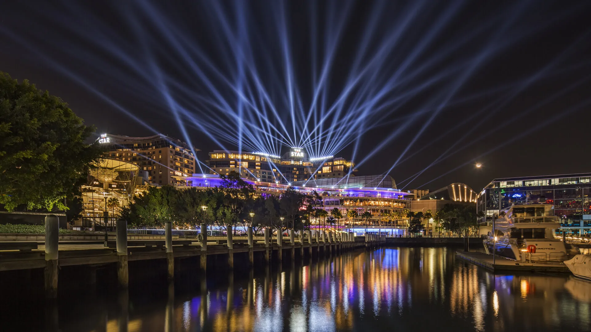 Blue light beams rise above The Star and reflect across the water during Vivid.
