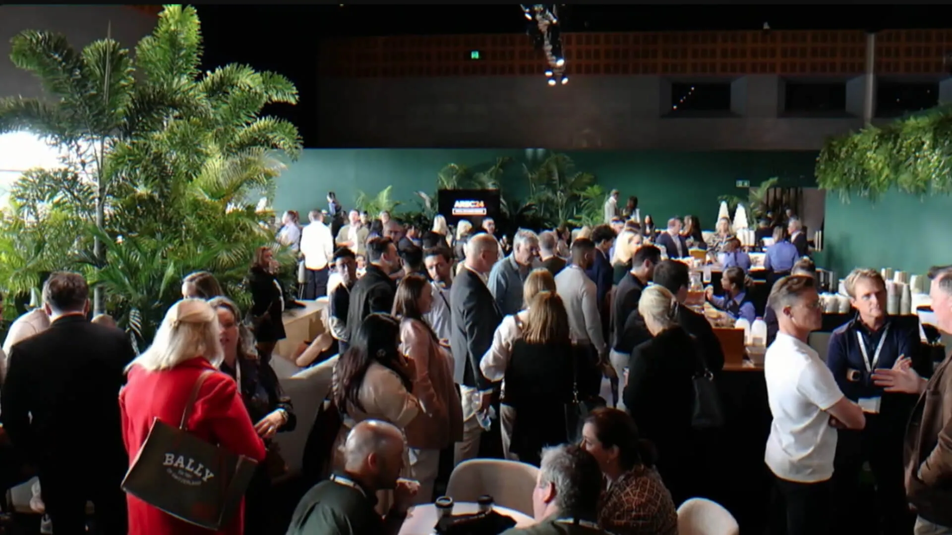 AREC delegates gather and talk in a reception space filled with indoor plants.