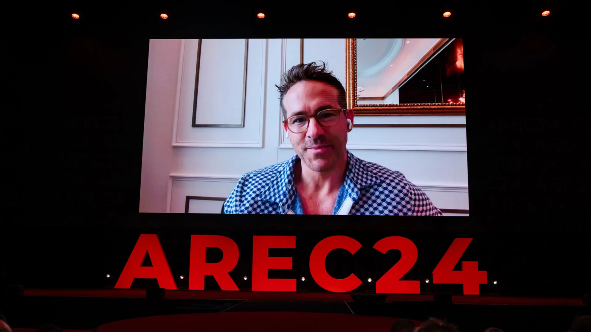Remote speaker appears on a large screen above red AREC24 lettering.