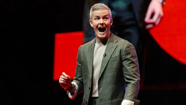 Speaker in a green jacket gestures on the AREC stage.