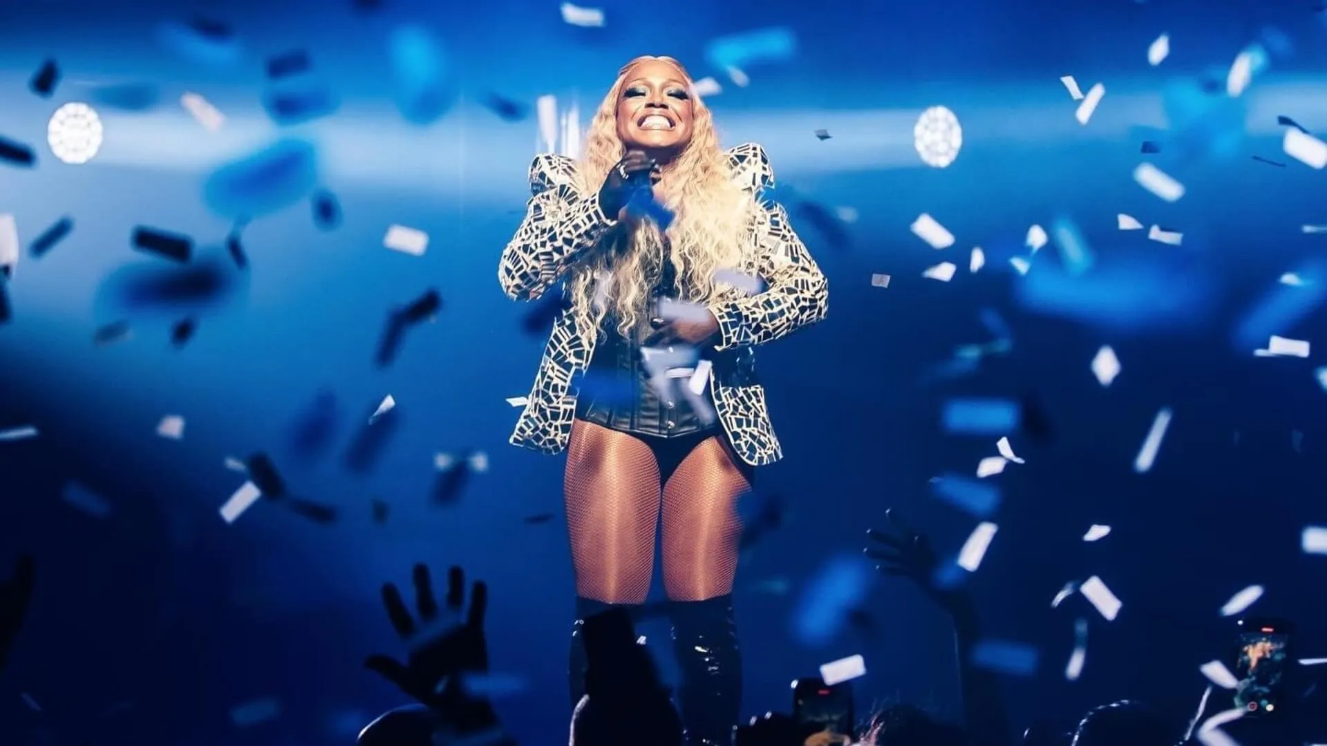 Singer performs amid falling confetti on a blue-lit Mardi Gras stage.