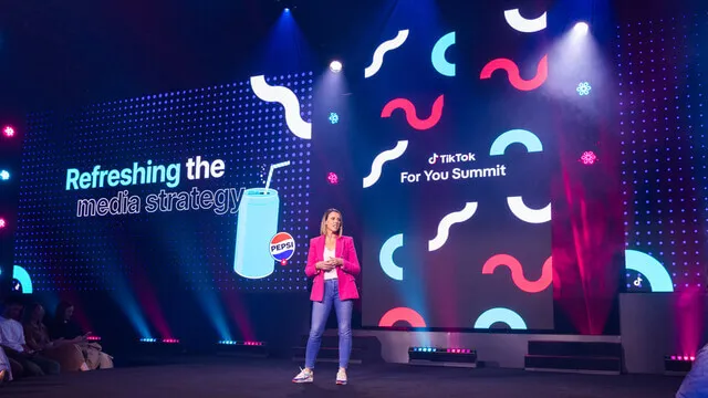 Presenter speaks beside the TikTok For You Summit screen and colourful graphics.