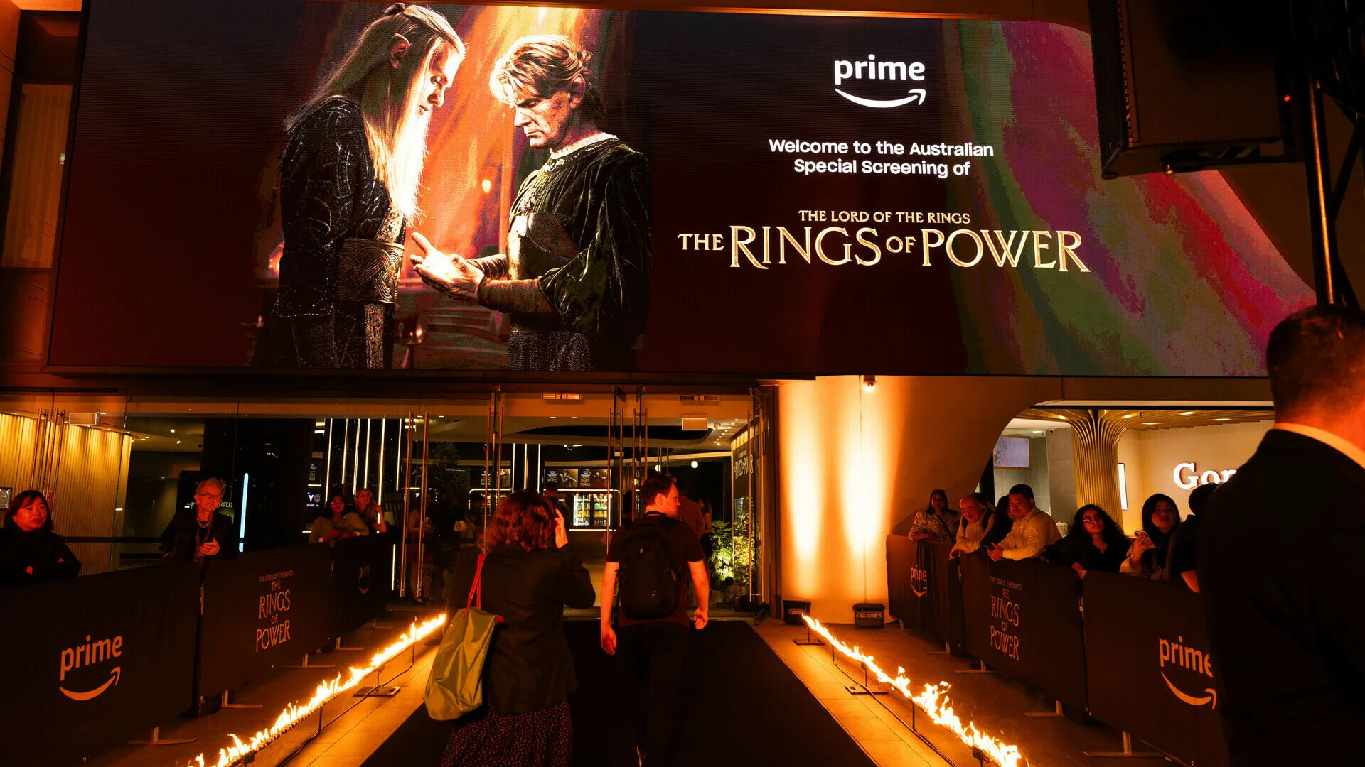 Guests enter a fire-lined walkway beneath a large Rings of Power screen.