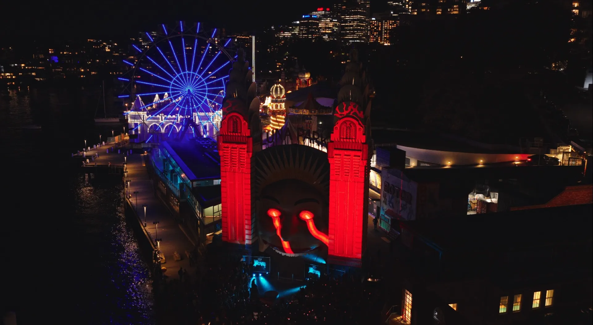 Luna Park entrance towers lit red beside a blue-lit Ferris wheel at night.