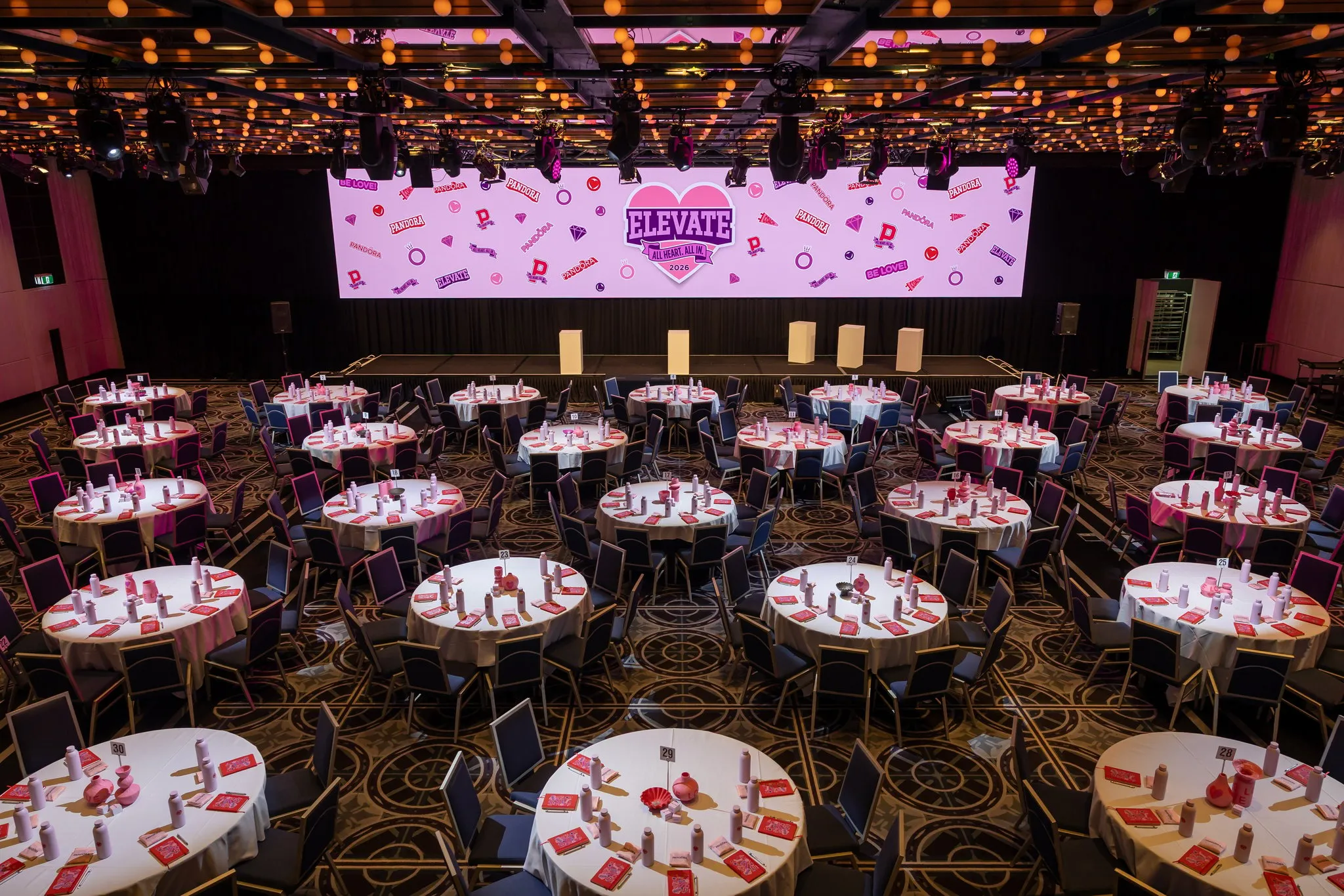 Round tables set beneath colourful ceiling lights and an ELEVATE screen at the Pandora conference.