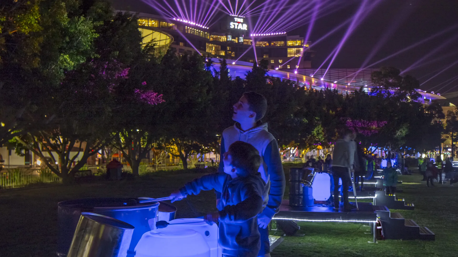 DJ performs outdoors beneath purple light beams at The Star during Vivid.