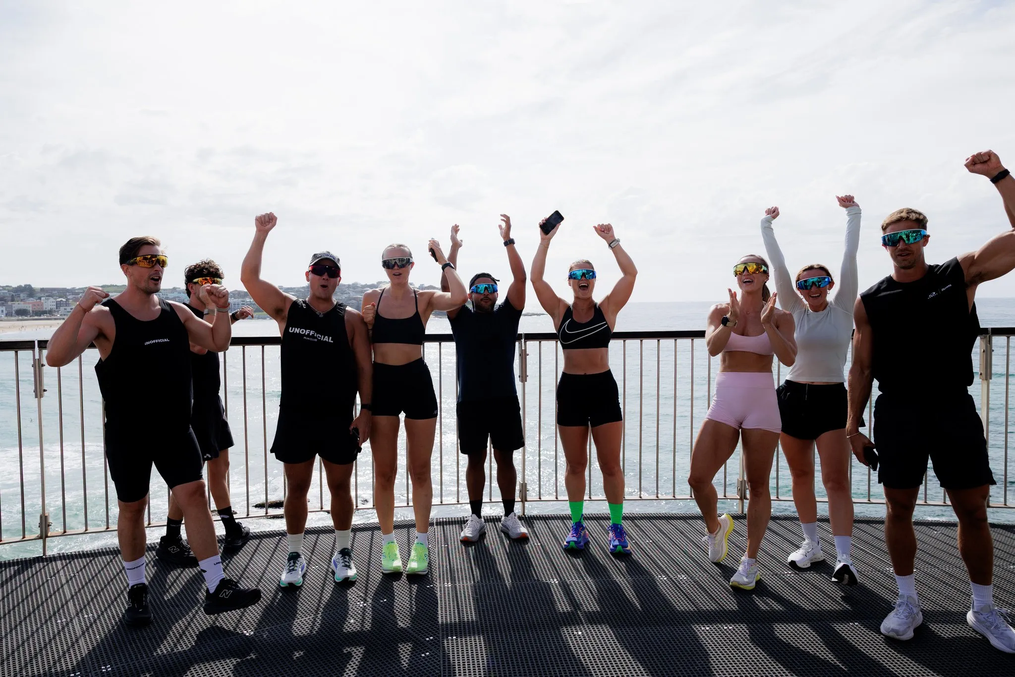 Group of participants poses beside the waterfront with their arms raised.