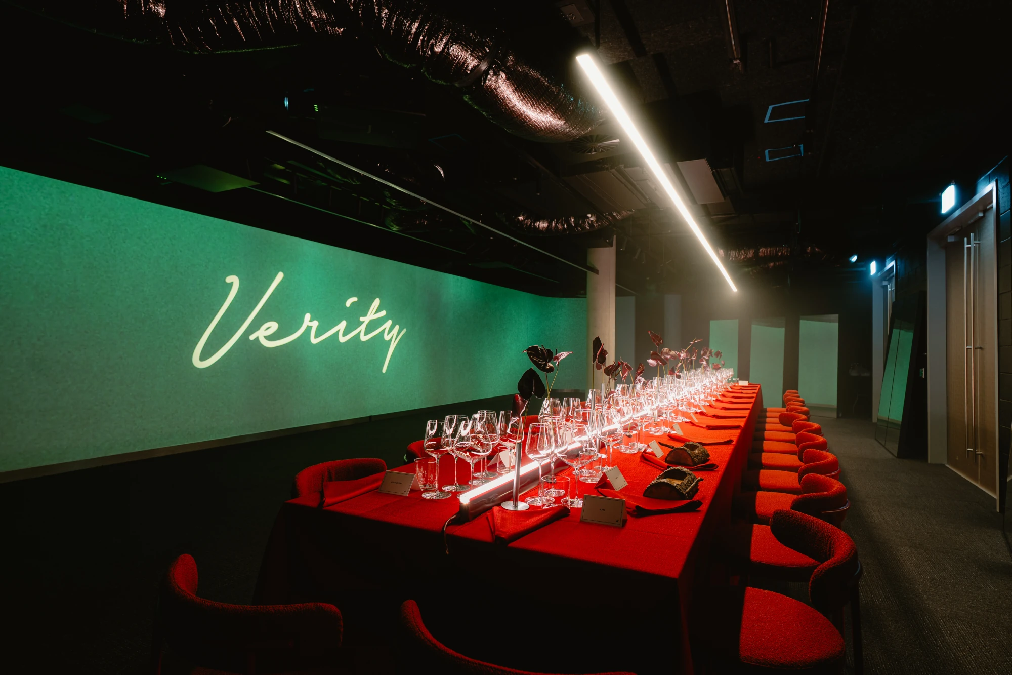 Red chairs and a long dining table face the green Verity backdrop.