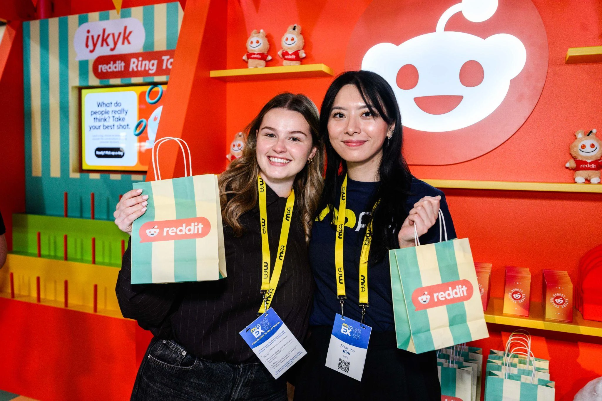 Two guests hold Reddit-branded bags in front of a colourful event backdrop.