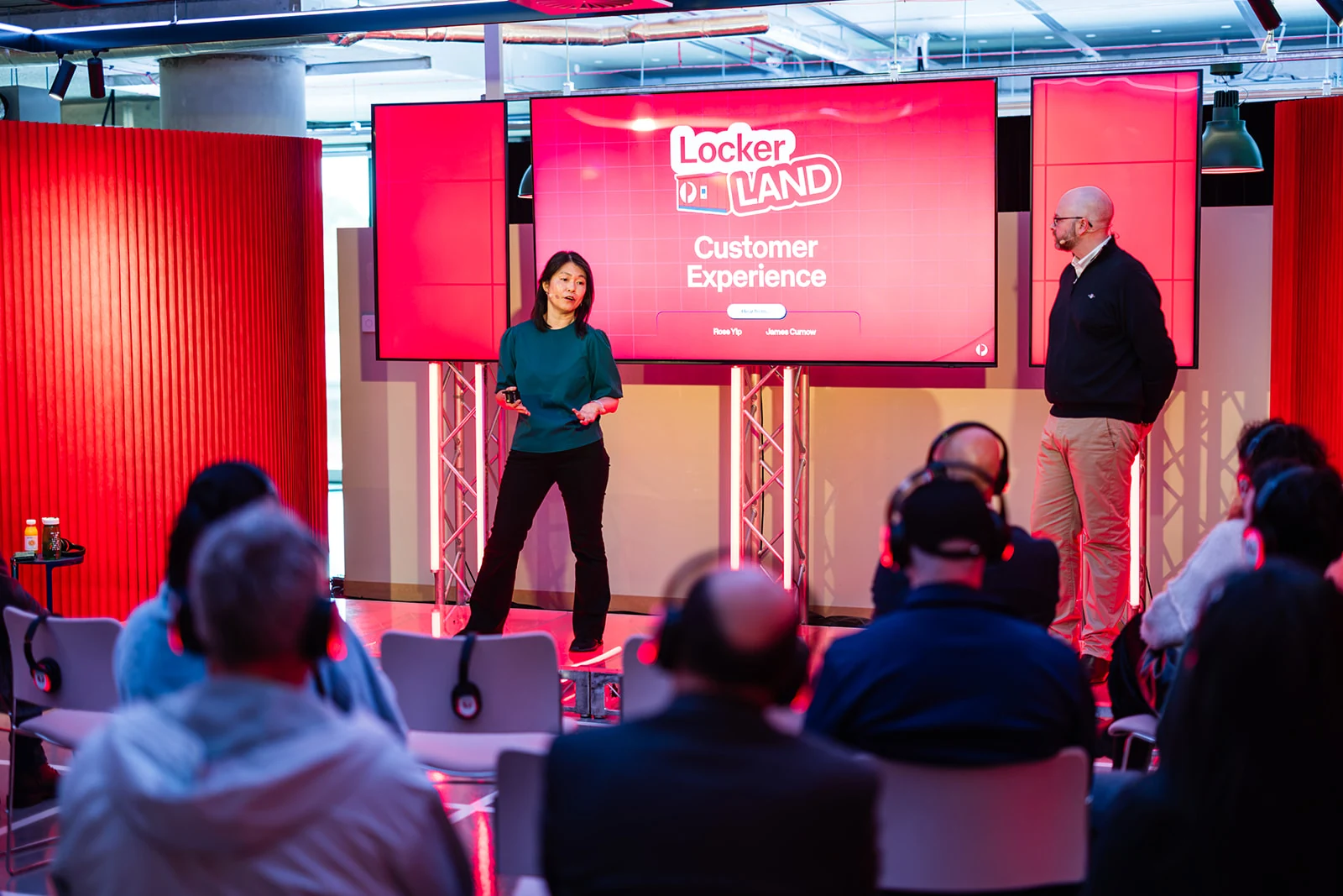 Two presenters speak to seated attendees beneath the Locker Land Customer Experience screen.