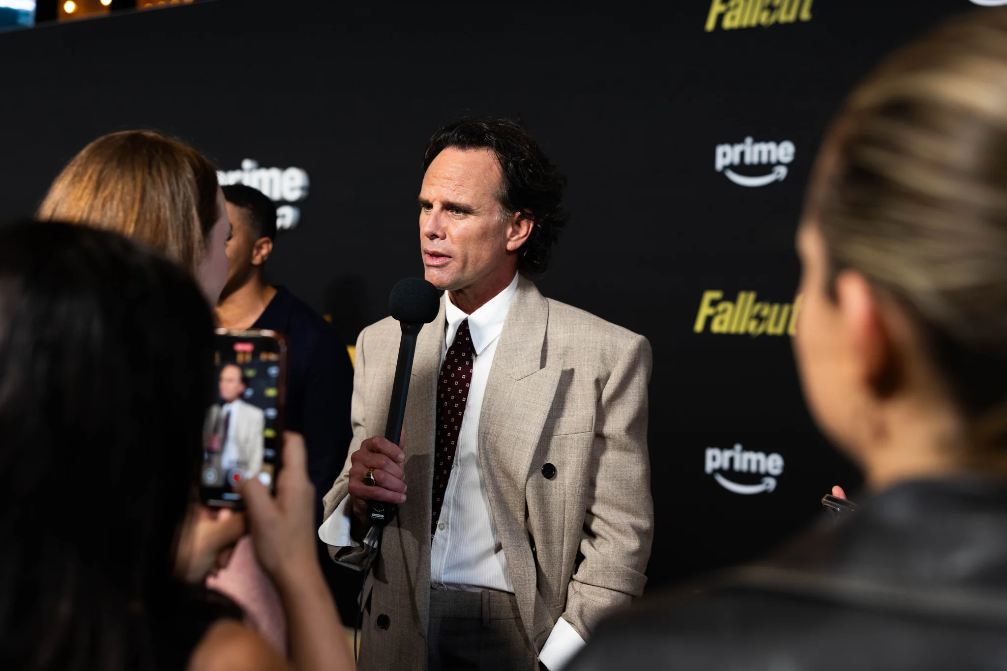 A cast member in a light suit speaks with media on the indoor Fallout red carpet.