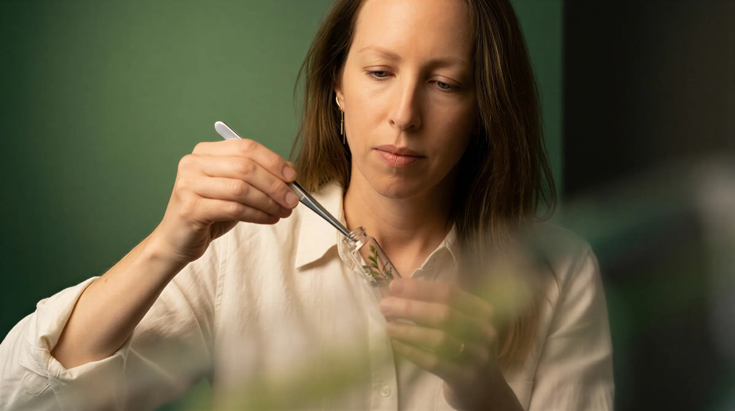 Focused woman using tweezers to place a plant sample into a glass test tube in a lab setting