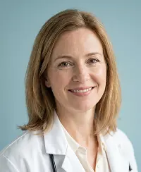 Smiling middle-aged female doctor with light brown hair wearing a white coat and stethoscope.