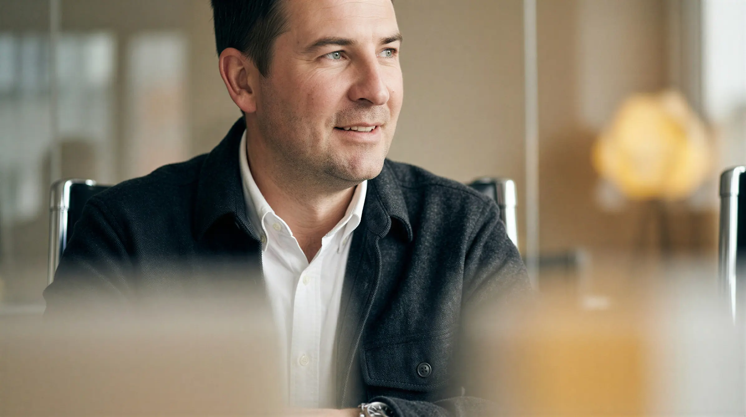 Thoughtful man in white shirt and dark jacket sitting in a modern office setting.