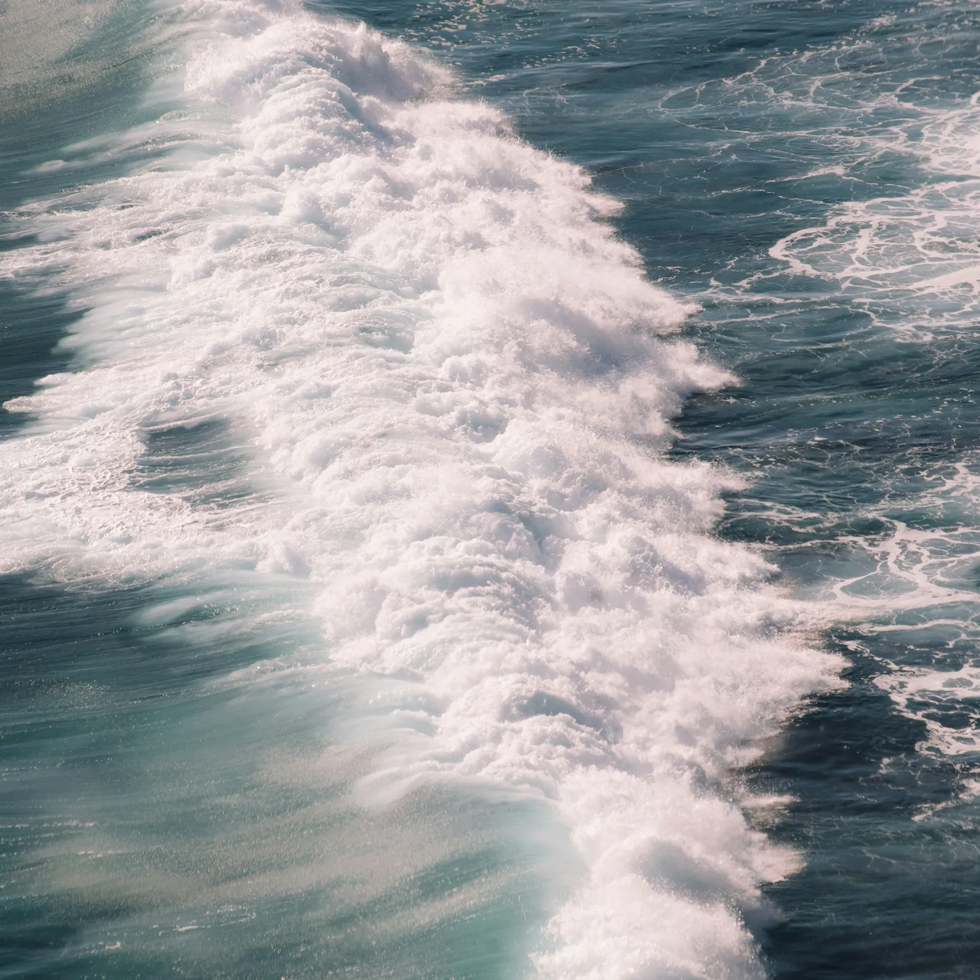 White churning foam and sea spray cutting across deep teal-blue ocean water.