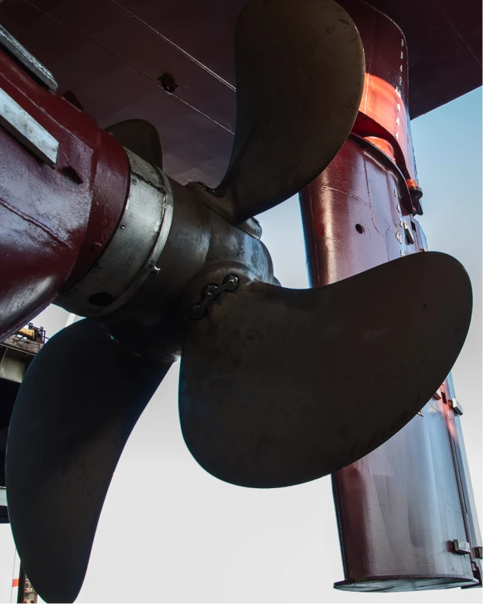 A large ship's bronze propeller and rudder viewed from below in dry dock.