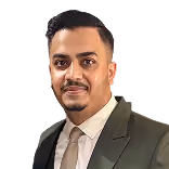 Man with short black hair and goatee wearing a dark suit jacket and light shirt.
