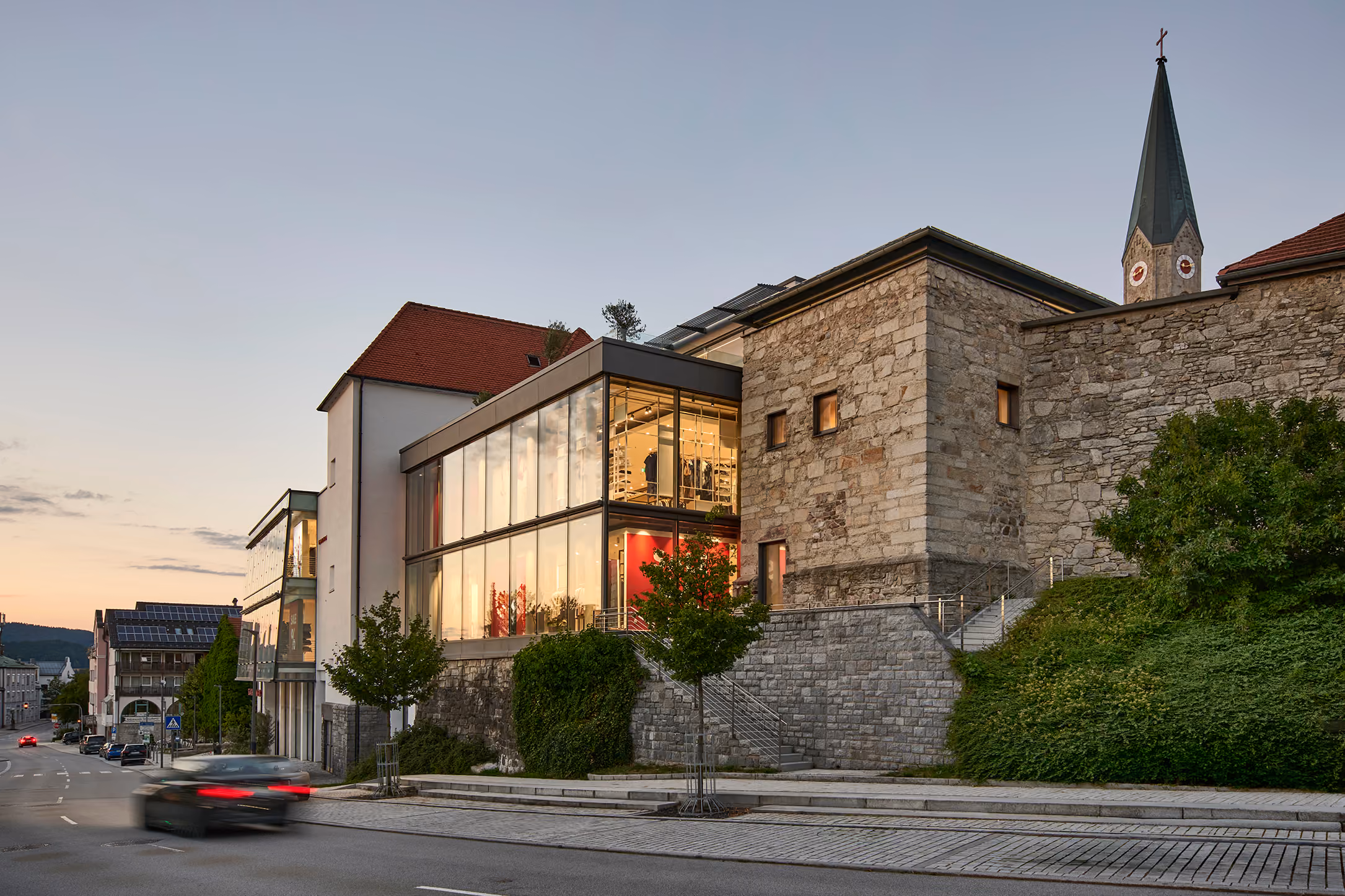 Modehaus GARHAMMER in Waldkirchen am Abend, Außenansicht mit Glasfassade und Kirchturm