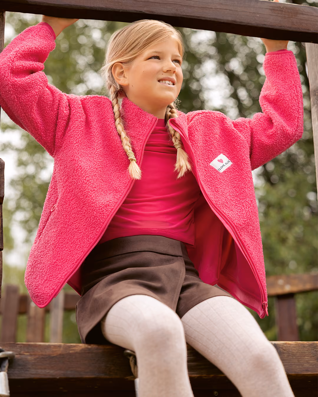 Mädchen in pinker Fleecejacke auf einem Holzgerüst