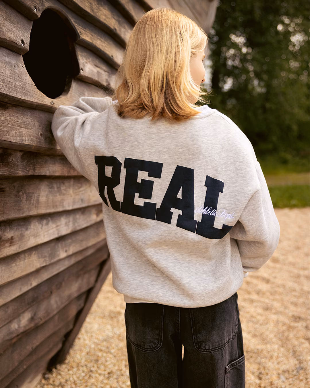 Kind in hellem Sweatshirt mit Aufdruck REAL von hinten