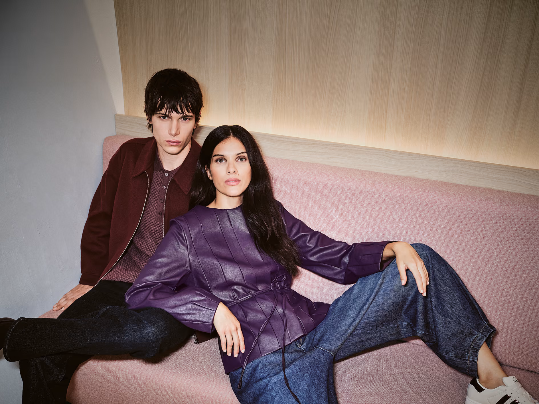 Zwei Models in bordeauxroter Jacke und violetter Lederbluse auf einem rosa Sofa