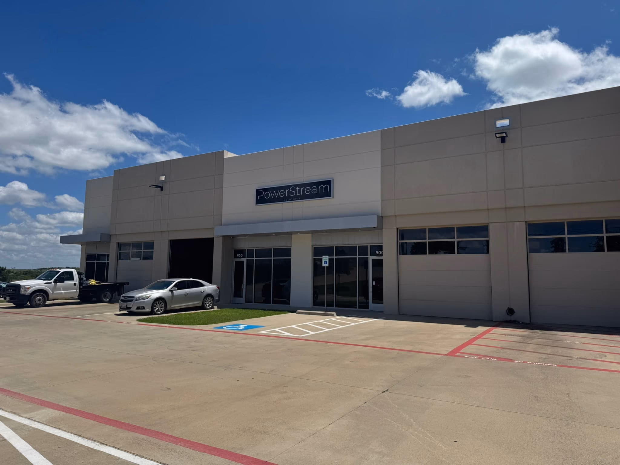 Exterior view of a beige commercial building under a blue sky with clouds, featuring a sign that reads PowerStream, with vehicles parked in front and a designated handicapped parking spot.