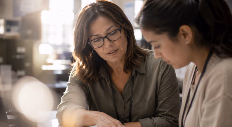 Two women working closely together and discussing something on a document in a warmly lit room.