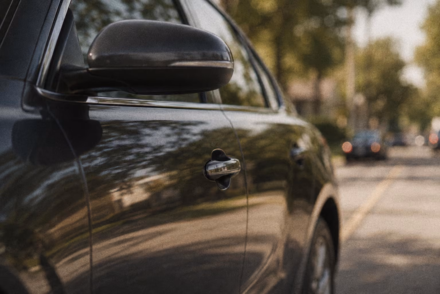 Close-up of black car's side mirror and door handle with blurred street background.
