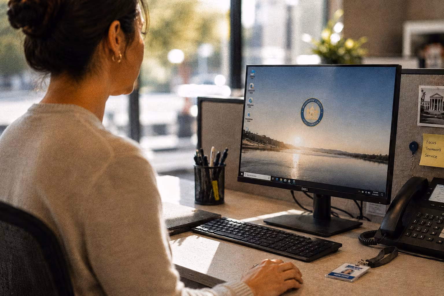 Woman sitting at a desk working on a computer with Riverside County California wallpaper on screen.