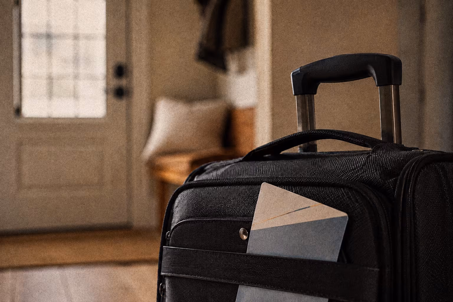 Black carry-on suitcase with a boarding pass in the front pocket, in a cozy home entryway.