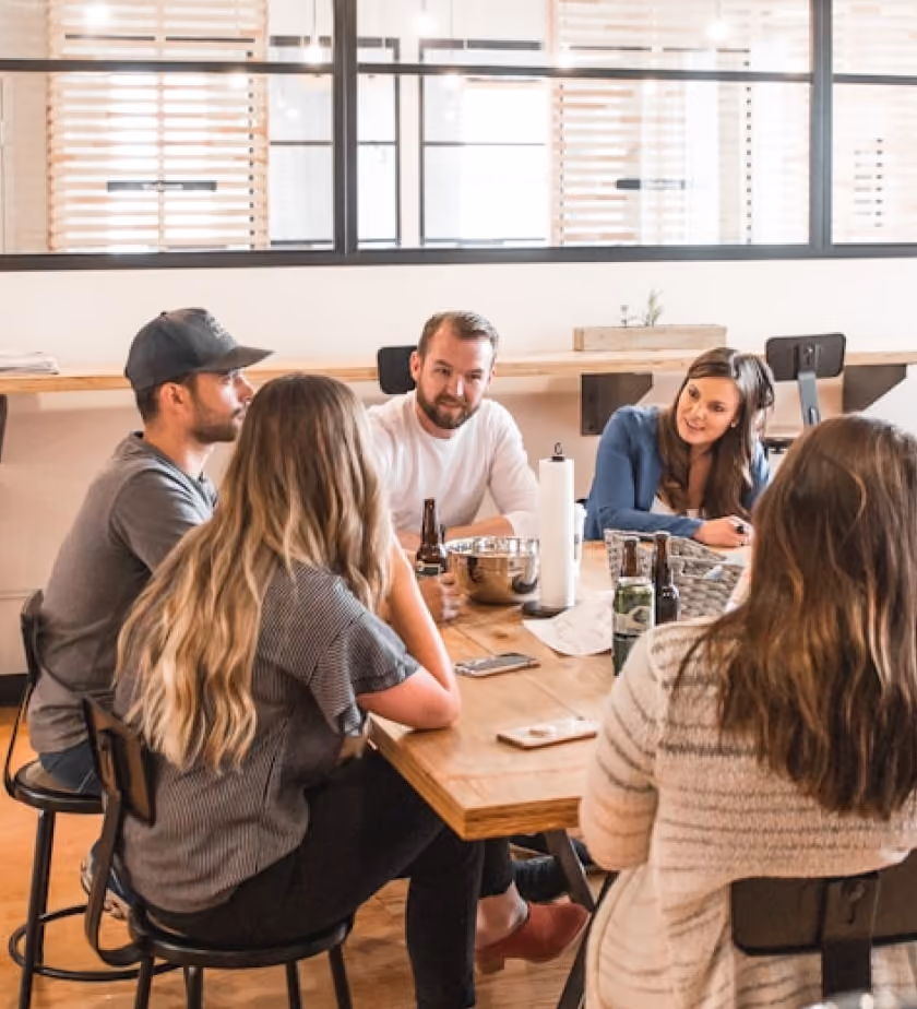 Five adults sitting around a wooden table having a conversation in a modern office space.