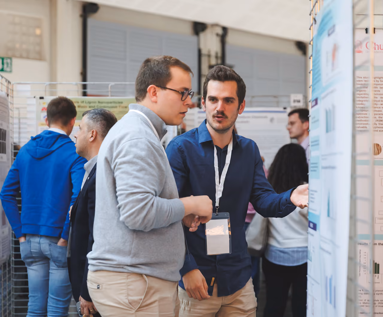 Two men discussing research posters at a conference or academic event indoors.
