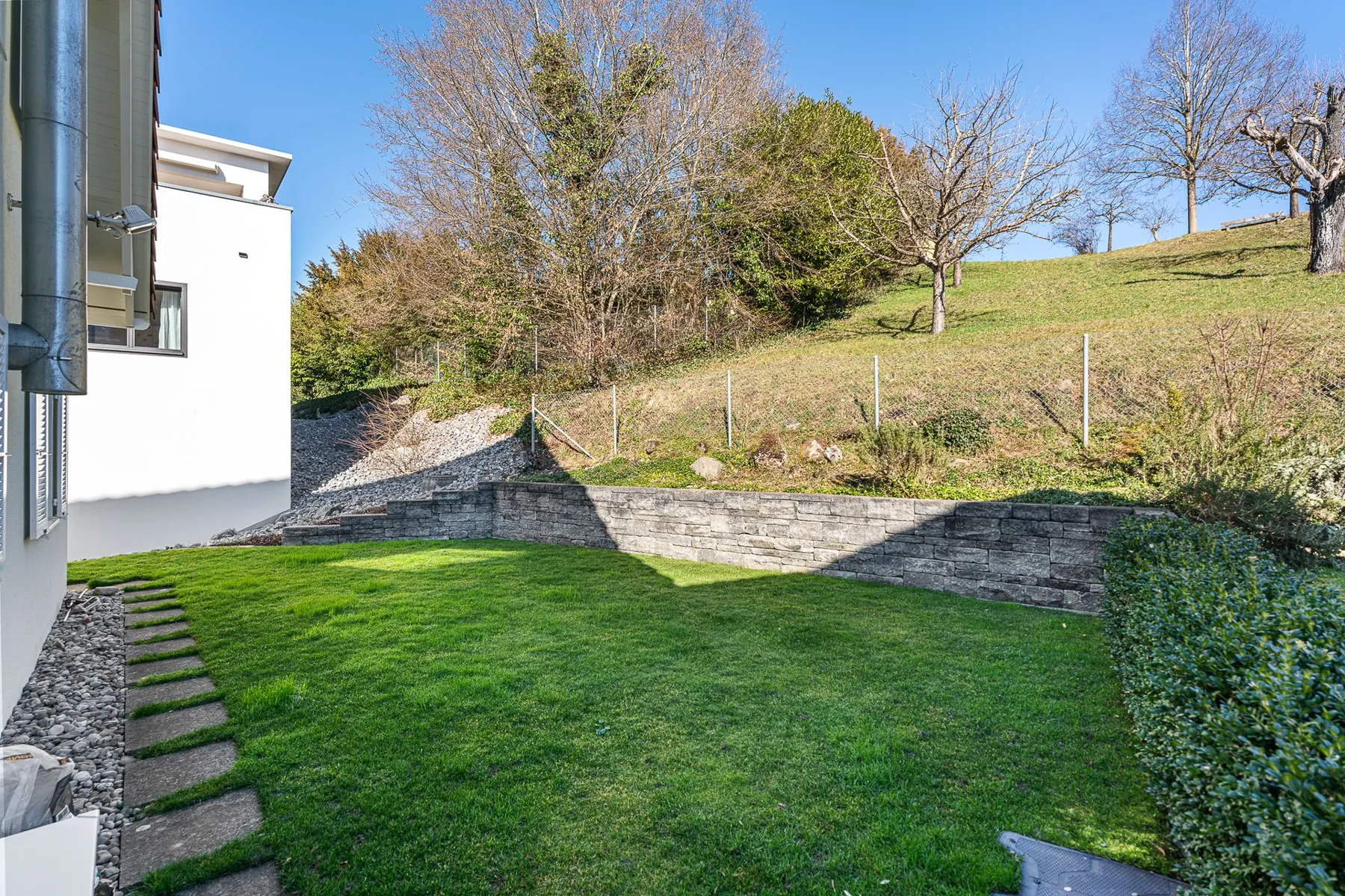 Garten mit Rasen, Steinmauer und Bäumen hinter dem Einfamilienhaus in Affoltern am Albis