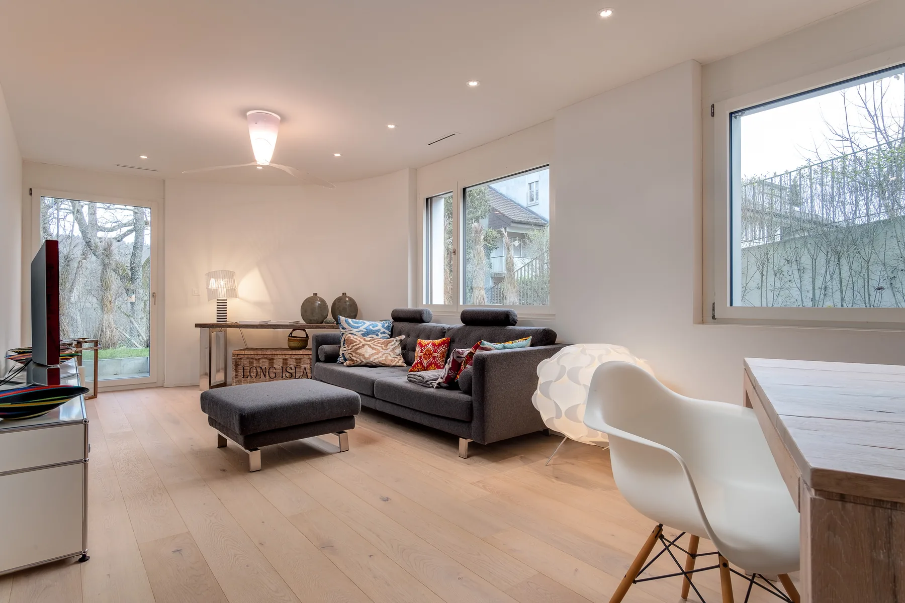 Wohnbereich mit grauem Sofa, grossen Fenstern und Gartentür in der Gartenwohnung an der Witikonerstrasse 486