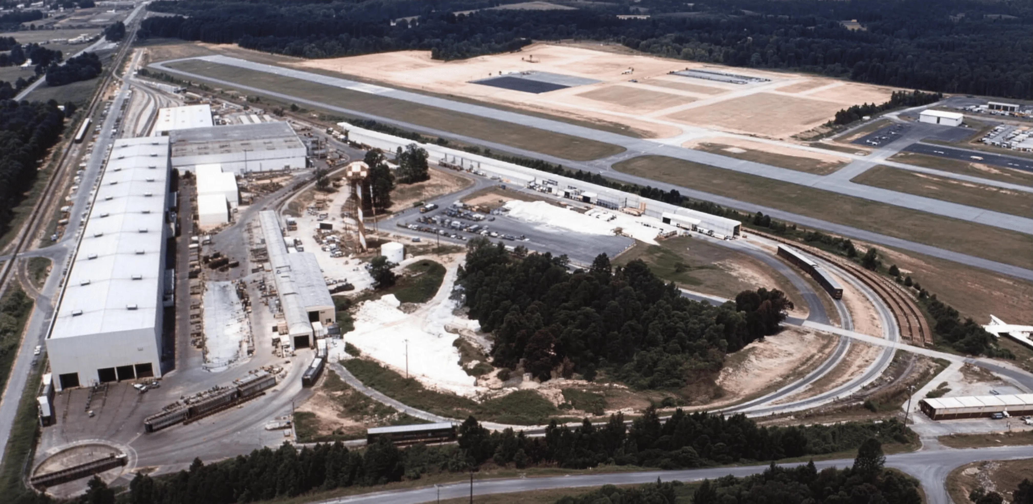 Aerial view of a manufacturing plant beside an airfield runway, 1980s
