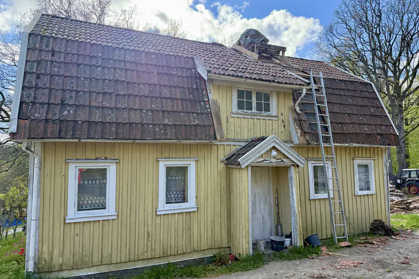 Samma hus före takbytet, med gammalt tegel och stege mot fasaden