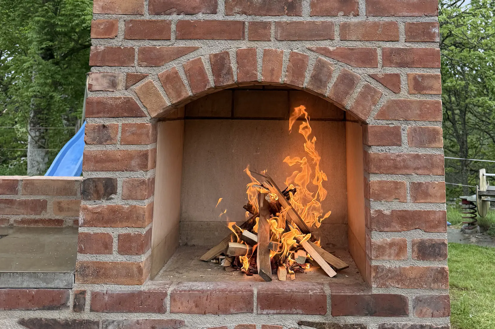 Närbild på eldstaden i den murade utegrillen, med första brasan brinnande