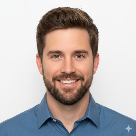 Smiling man with short brown hair and beard wearing a blue collared shirt against white background.
