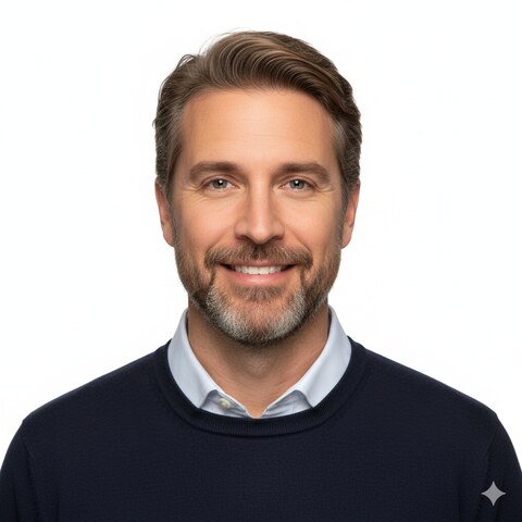 Smiling middle-aged man with brown hair and a beard wearing a navy sweater and white shirt.