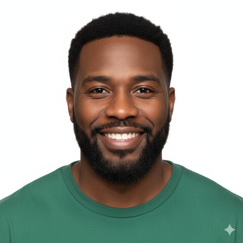 Smiling Black man with beard and short hair wearing a green shirt against a white background.