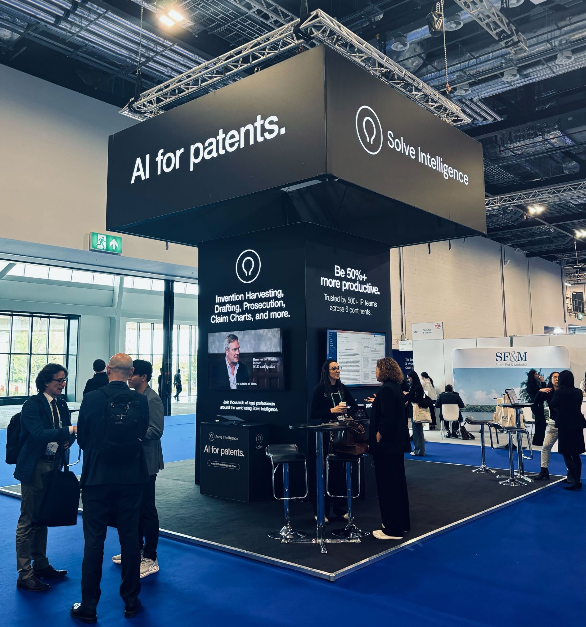 Solve Intelligence exhibition stand at a trade show, displaying “AI for patents” and “Be 50%+ more productive” signage, with attendees talking at the booth